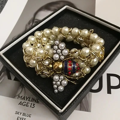 Pearl and gold brooch on a black box with Mayline makeup packaging in the background