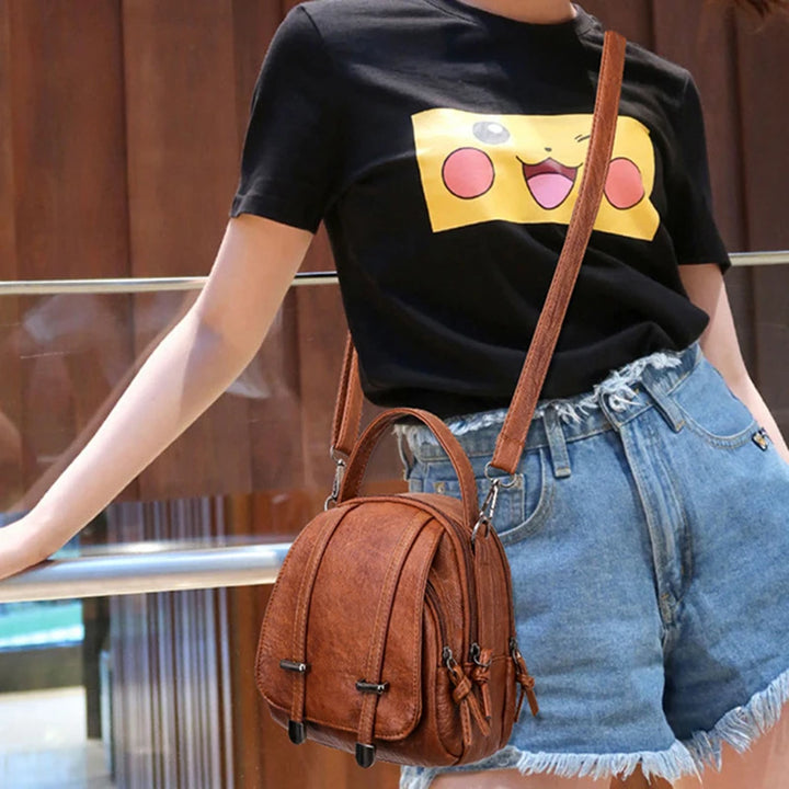 Person wearing a black t-shirt with a graphic design, blue jeans, and carrying a brown leather bag.