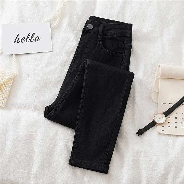 Folded black jeans on a textured white surface with a 'hello' card and watch.
