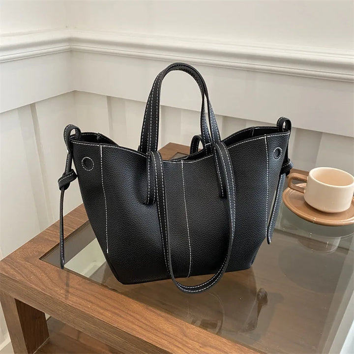 Black handbag on a wooden surface with a white wall background