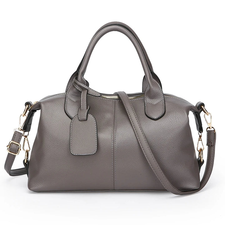 Gray soft leather tote bag with top handles, front luggage tag, and crossbody strap