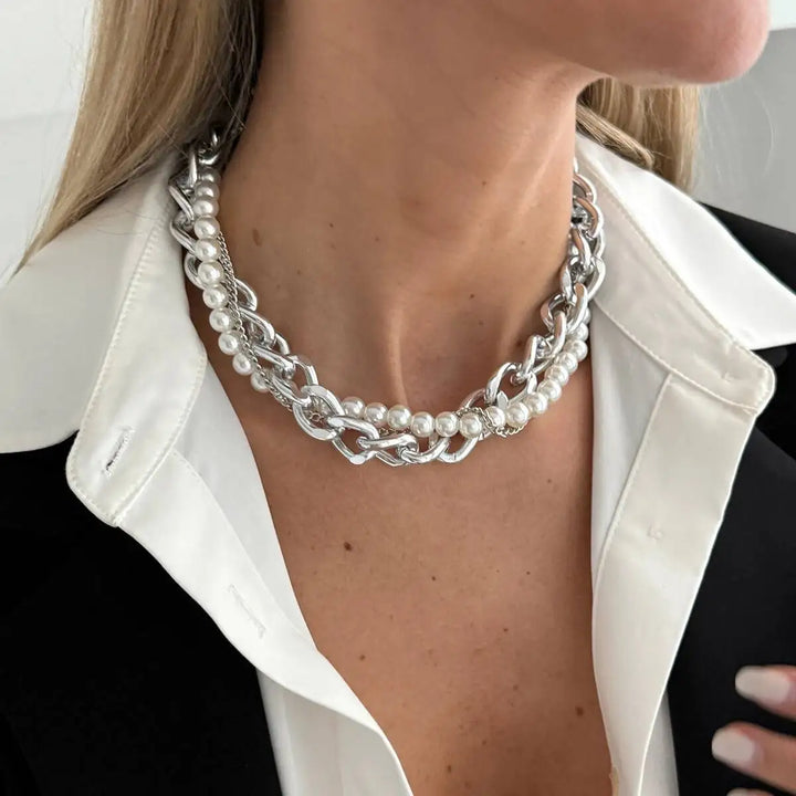 Close-up of a person wearing a silver chain and pearl necklace with a white blazer.