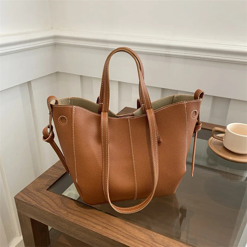Brown leather tote bag on a glass table with a white wall background