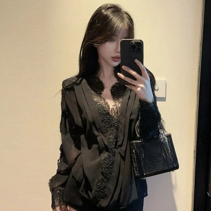 Woman taking a mirror selfie wearing a black lace top and holding a black handbag.