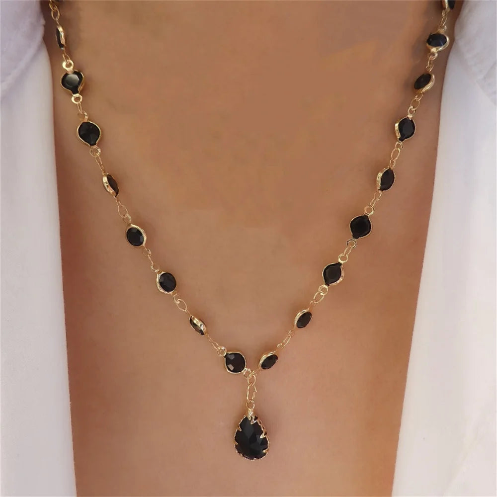 Gold-tone beaded necklace with black oval stones and a large central black teardrop pendant.