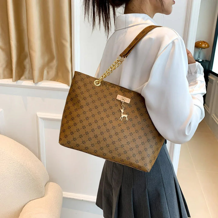 Women’s leather tote bag in brown monogram plaid with gold chain shoulder strap, side view.