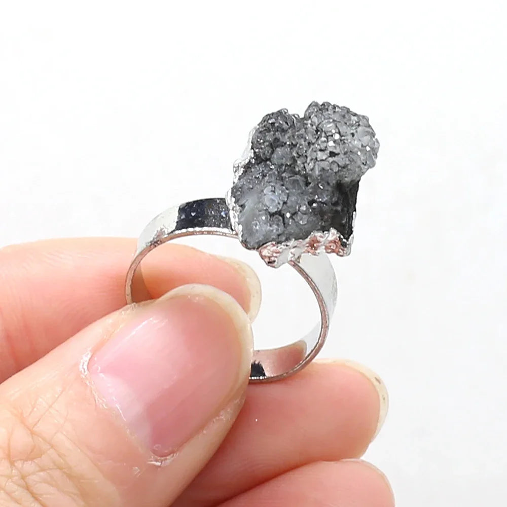 Silver ring with a gray crystal held between fingers against a white background