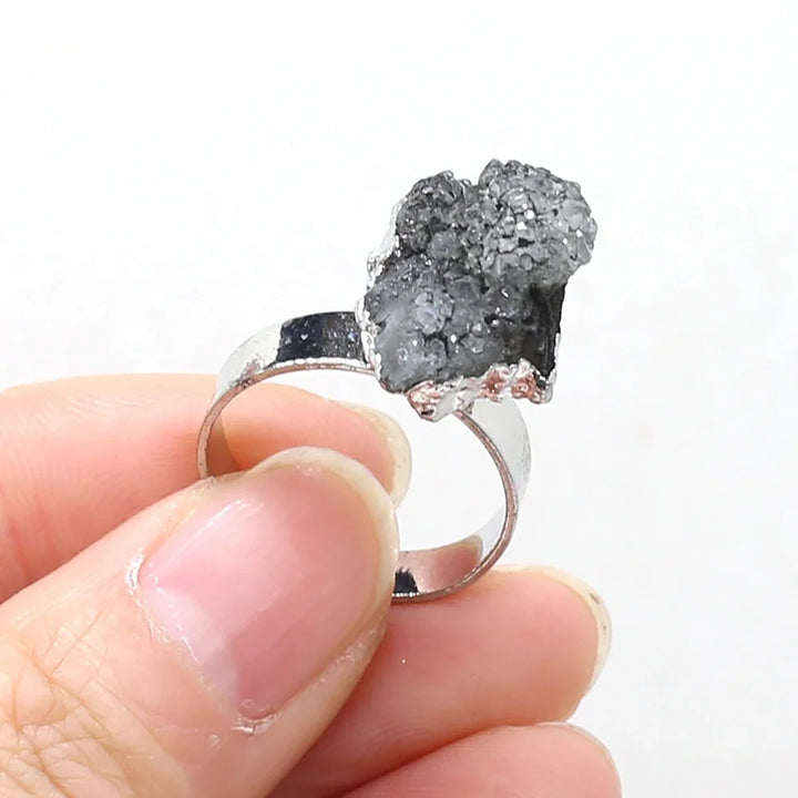 Silver ring with a gray crystal held between fingers against a white background