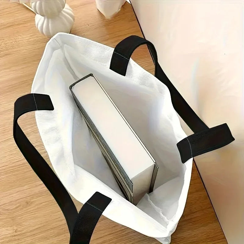 White canvas shoulder tote bag with black handles, open top showing interior pocket