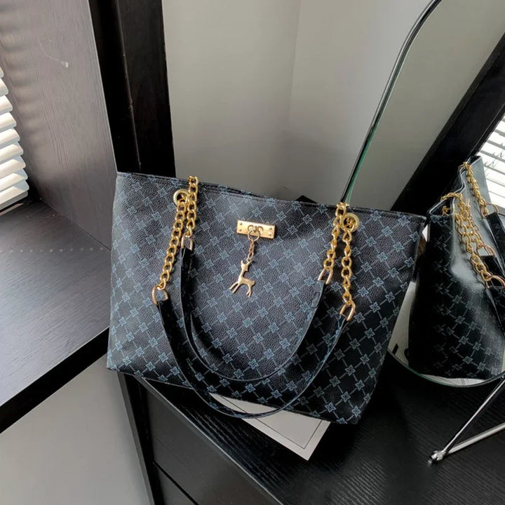 Women’s leather tote bag in dark blue monogram plaid, gold chain handles, hanging charms.