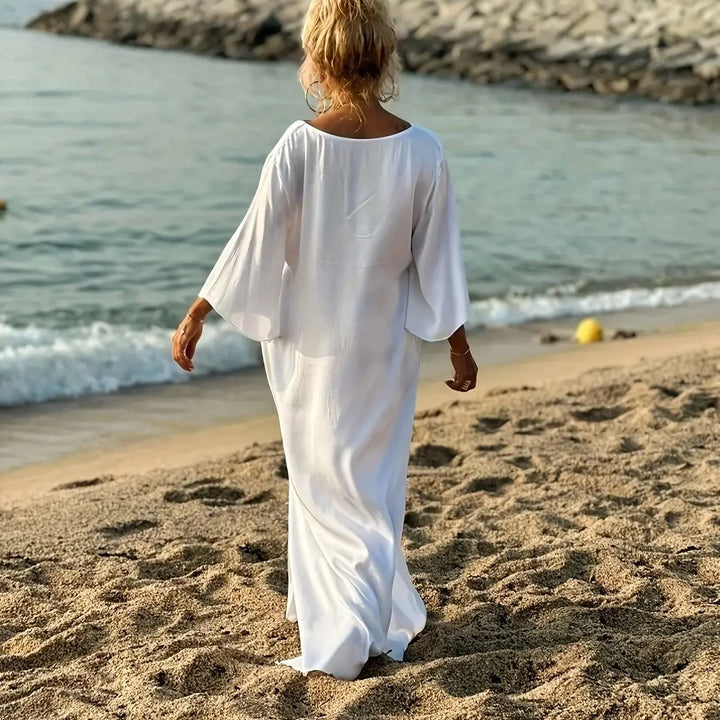 Woman in a white dress walking on a beach with waves in the background