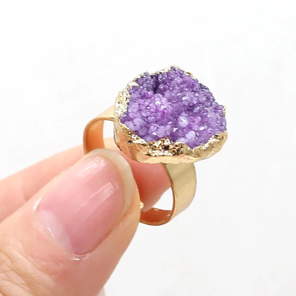 Gold ring with a purple geode stone held by a hand on a white background