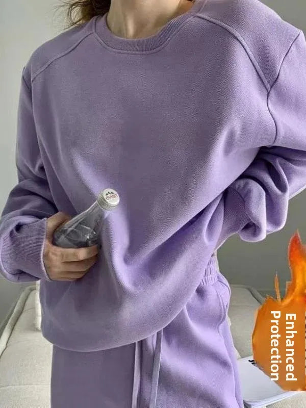 A person wearing an oversized lavender sweatshirt and matching sweatpants, holding a clear bottle. The image has a flame graphic overlay on the bottom right with the text 'Enhanced protection'.