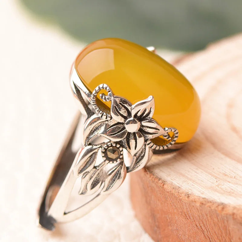Silver ring with floral design and yellow stone on a wooden surface