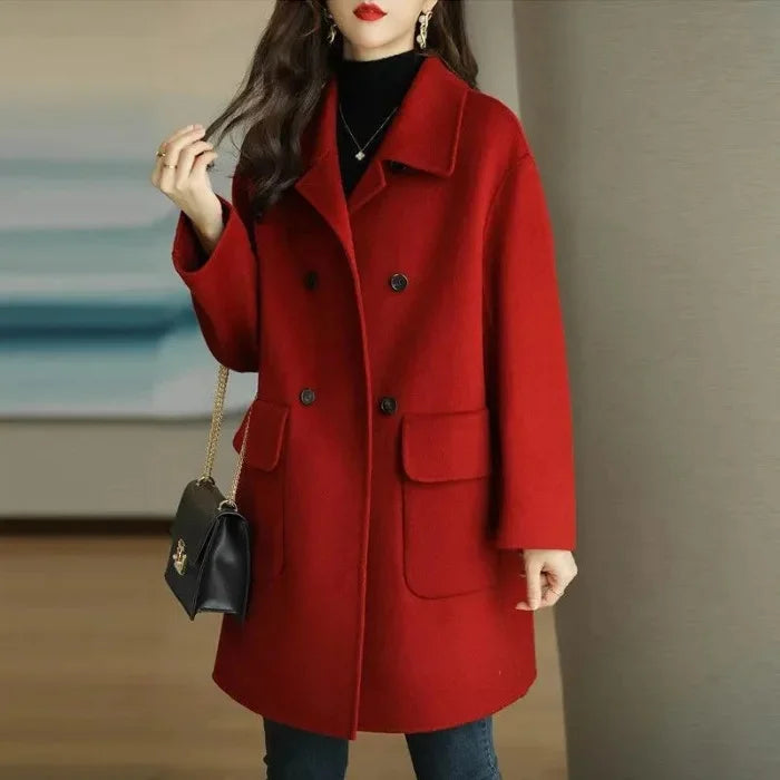 Person wearing a red coat holding a black handbag indoors.