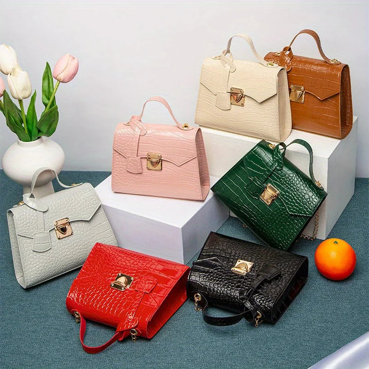 Collection of colorful handbags on a white surface with a vase of flowers and an orange.