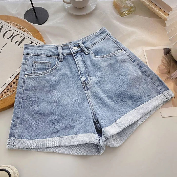 Light blue denim shorts on a white surface with a magazine and cup in the background