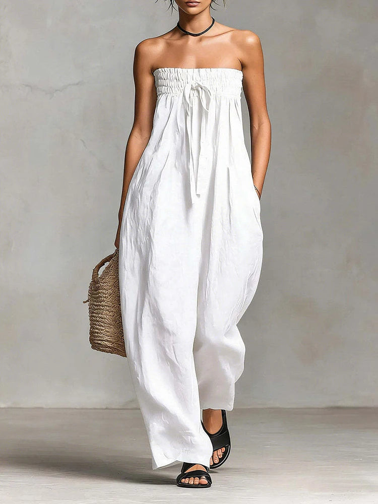 Woman wearing a strapless white dress holding a woven bag against a plain background