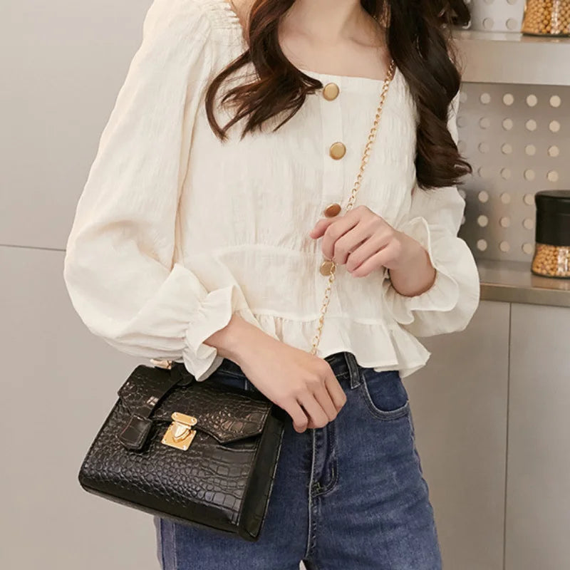 Person wearing a white blouse with gold buttons and blue jeans, holding a black handbag.