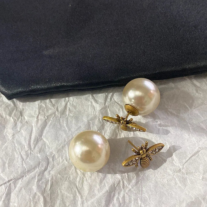 Pearl earrings with gold bee accents on a textured surface