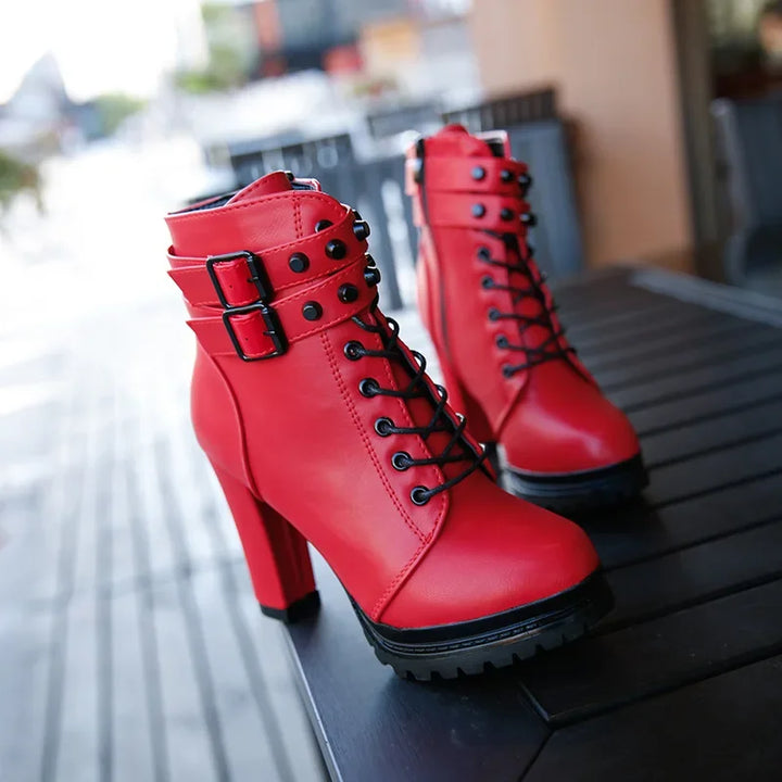Red high-heeled boots with black buckles on a wooden surface.