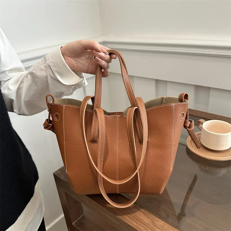 Brown leather handbag held by a person with a neutral background
