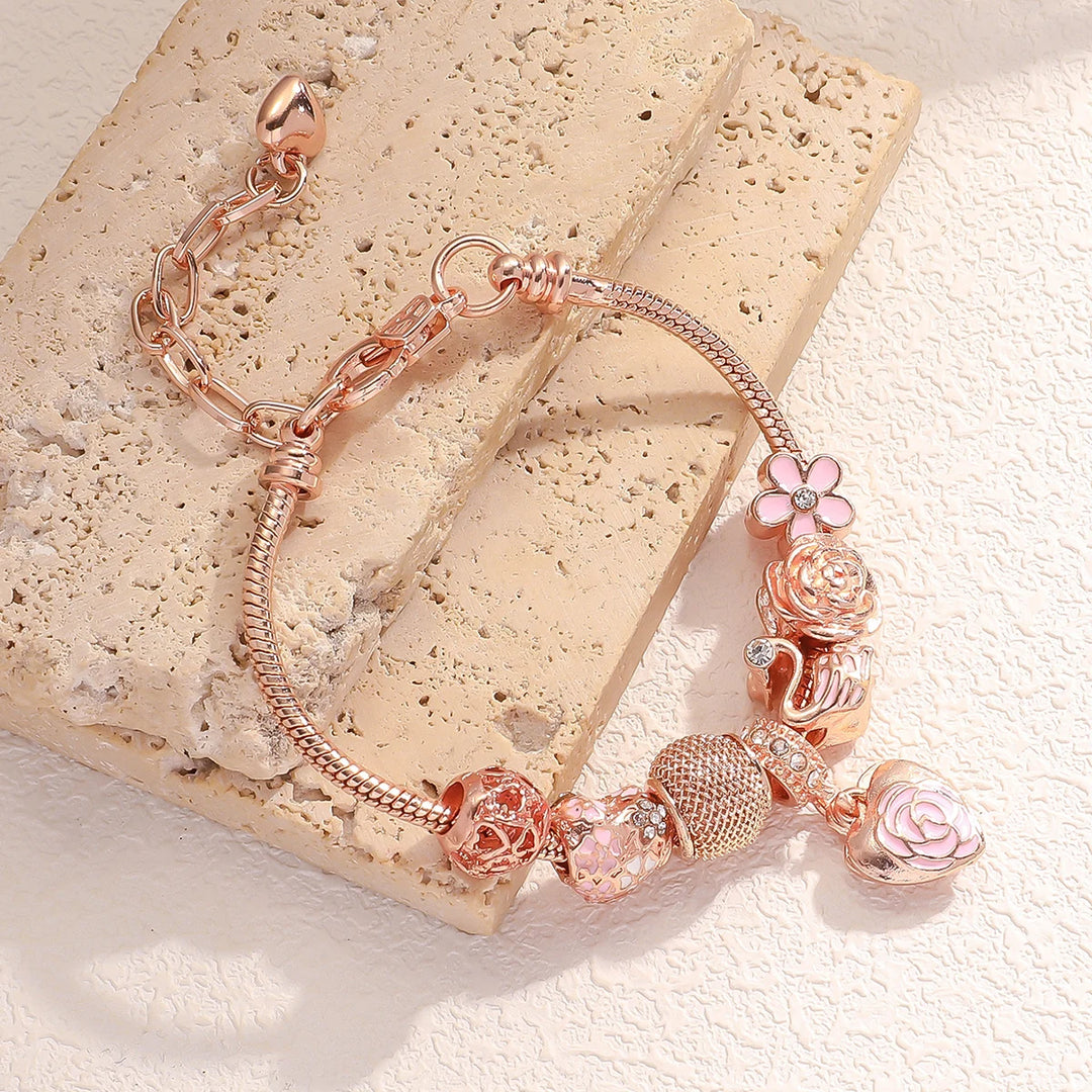 Rose gold charm bracelet with rose, flower, and heart dangle charms on a snake chain