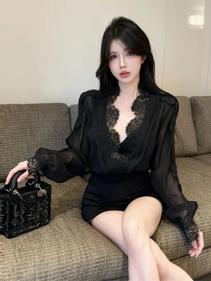 Woman in a black lace dress sitting on a couch holding a black handbag.
