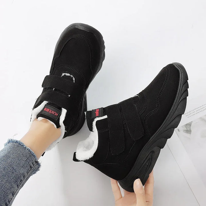 Black winter boots with white fur lining held by a person on a light gray background