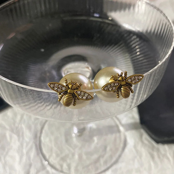 Hand wearing a decorative ring with a bee design on a neutral background