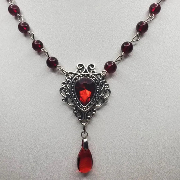 Close-up of gothic bead necklace: dark red beads, filigree centerpiece with red stone