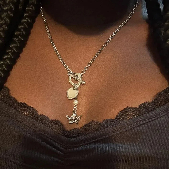 Necklace with heart and angel pendant on a person wearing a dark brown top.