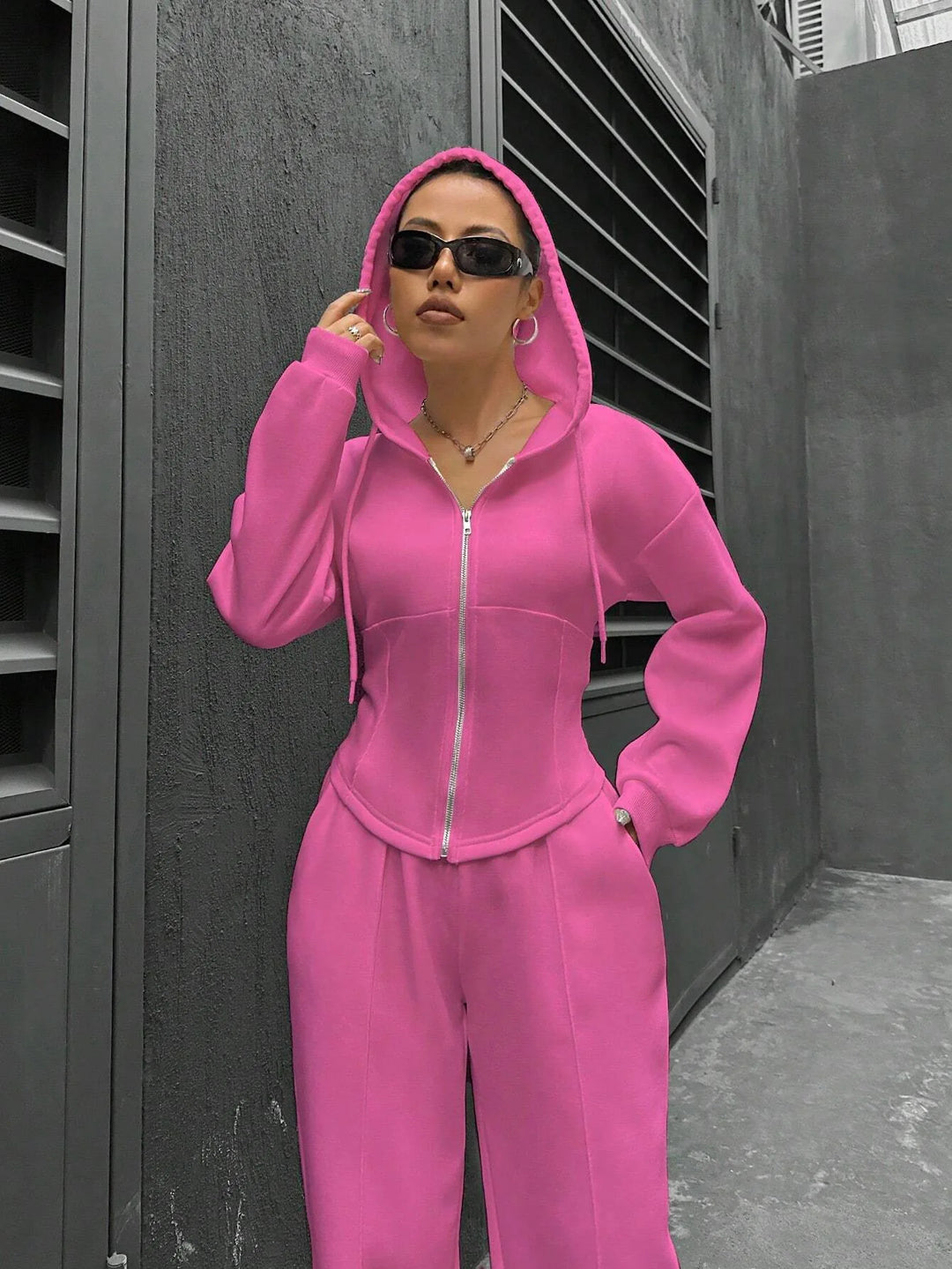 Person wearing a pink tracksuit standing against a dark wall.