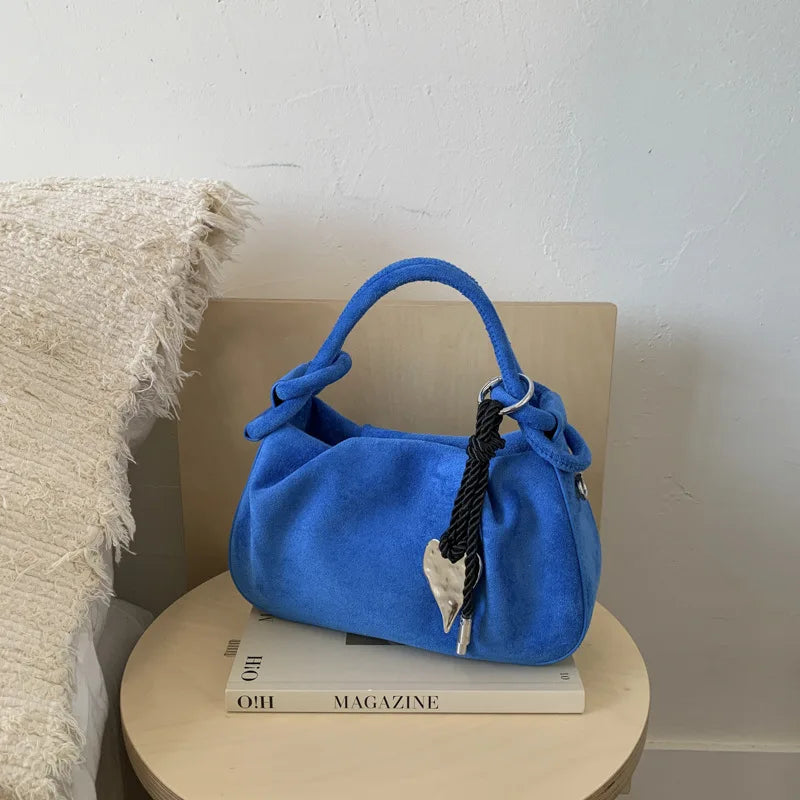 Blue suede mini hobo crossbody bag with short handles, braided cord, and heart charm.