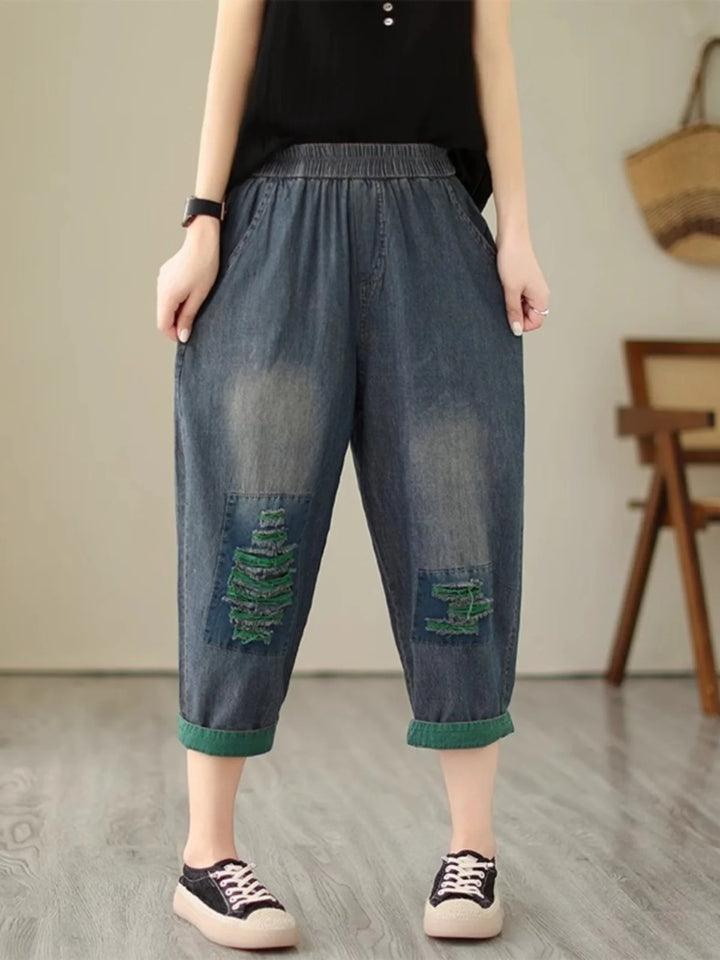 Person wearing blue denim capri pants with green patches in a room setting.
