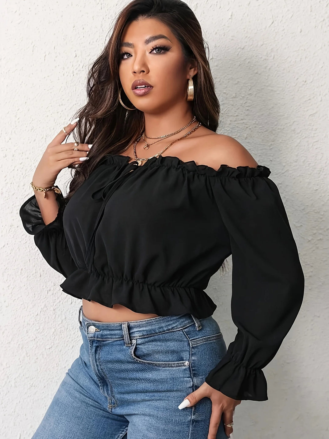 Woman wearing a black off-shoulder top and blue jeans against a white background