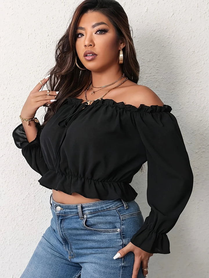 Woman wearing a black off-shoulder top and blue jeans against a white background