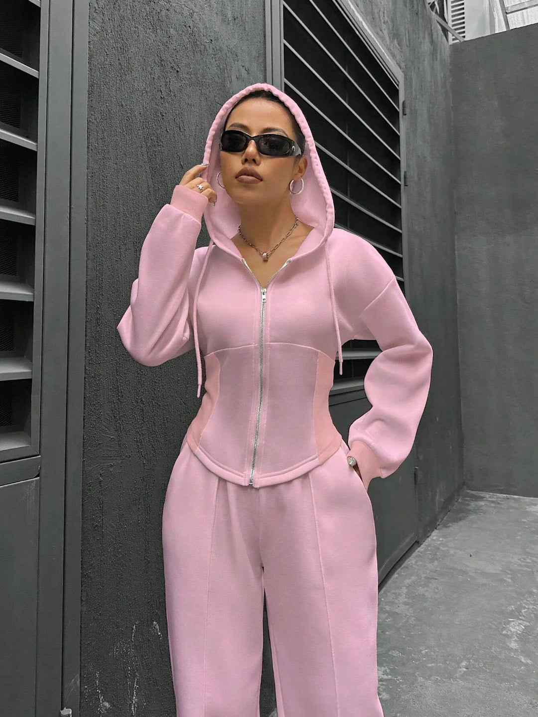 Person wearing a pink tracksuit standing against a gray wall.