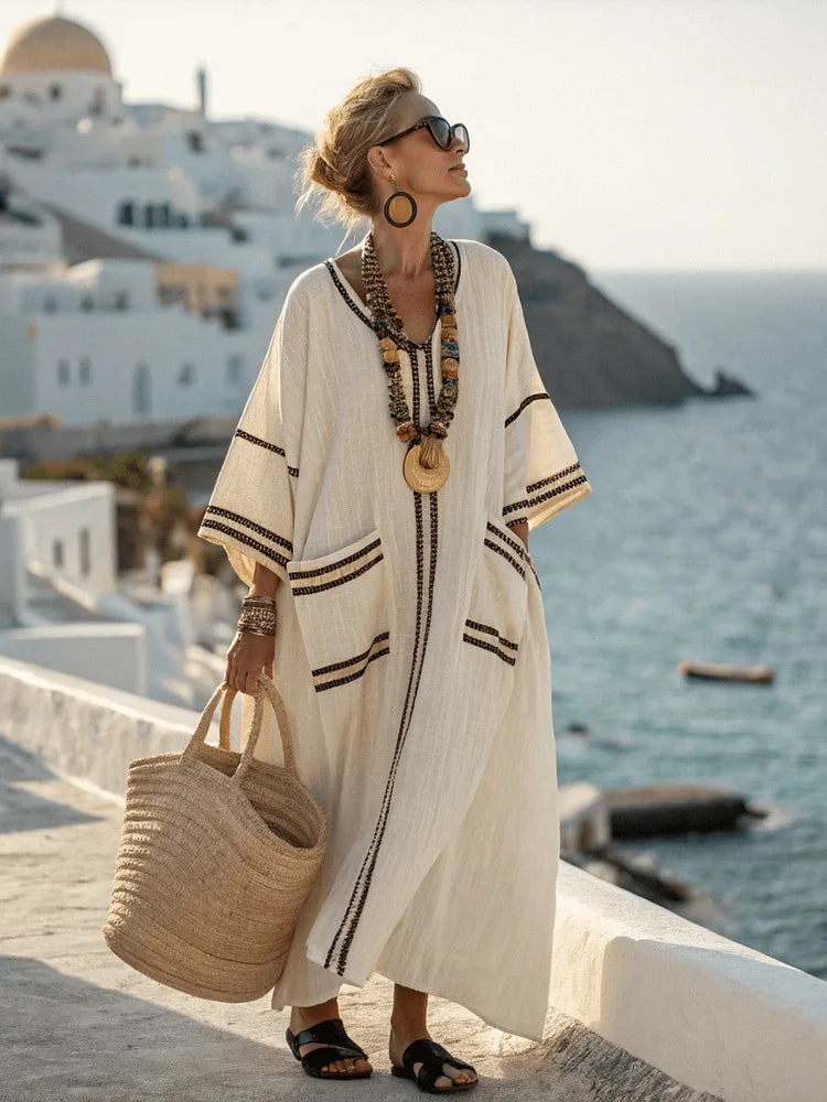Woman in a white dress with black stripes standing on a scenic coastal path.