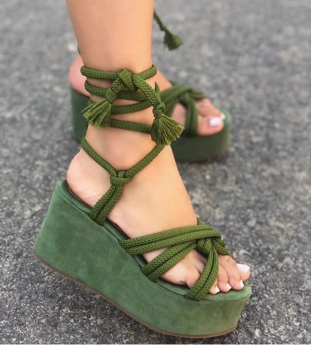 Green wedge sandals with knotted straps on a gray pavement background