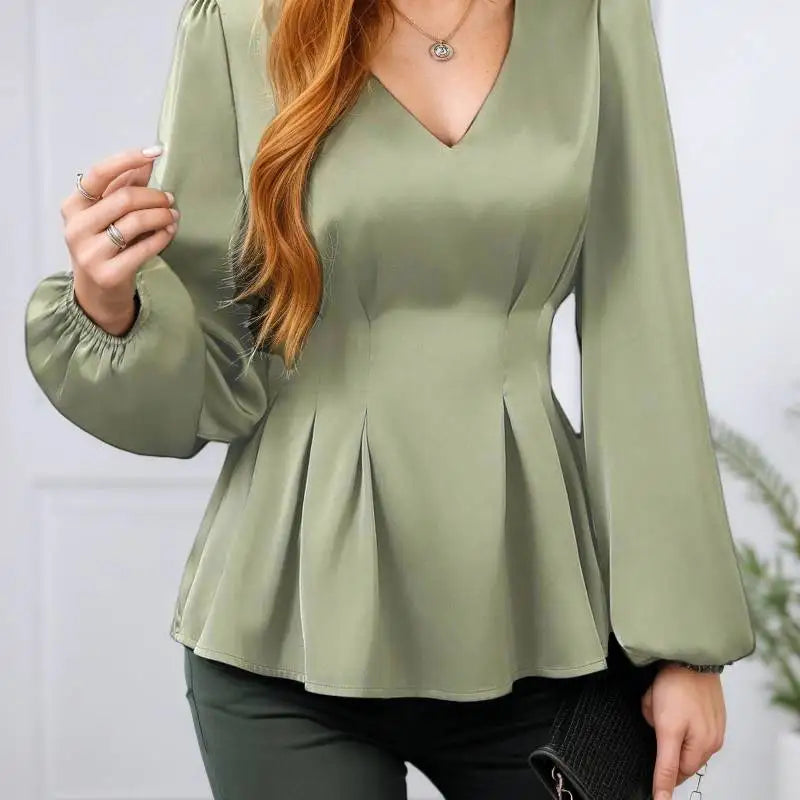 Person wearing a green peplum top with long sleeves against a white background