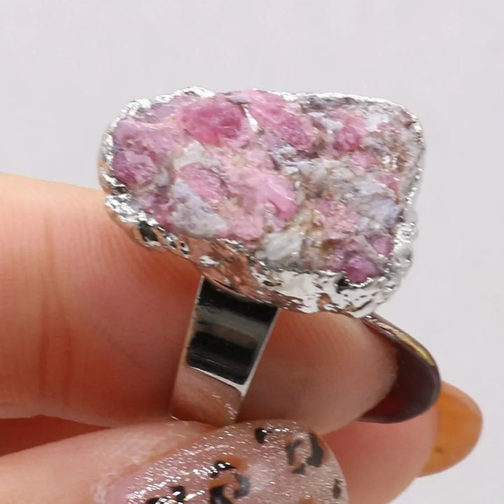 Ring with pink stone held on a finger against a white background