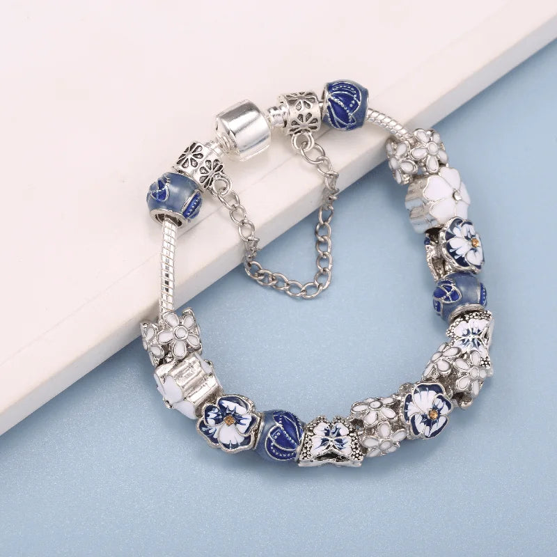 Silver butterfly charm bracelet with blue beads, white flowers, and a round clasp