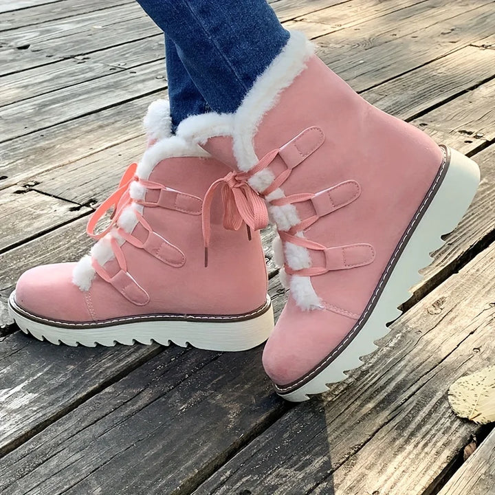 Pink winter boots with white fur trim on a wooden floor