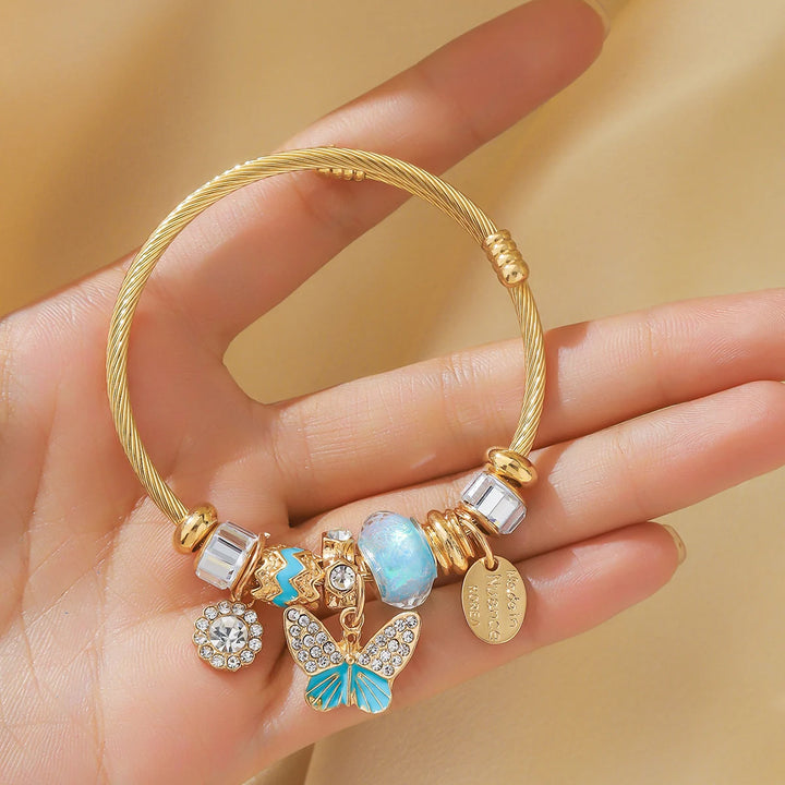 Goldfarbener Armreif mit blauem Stein, Schmetterlings- und Blumenanhängern