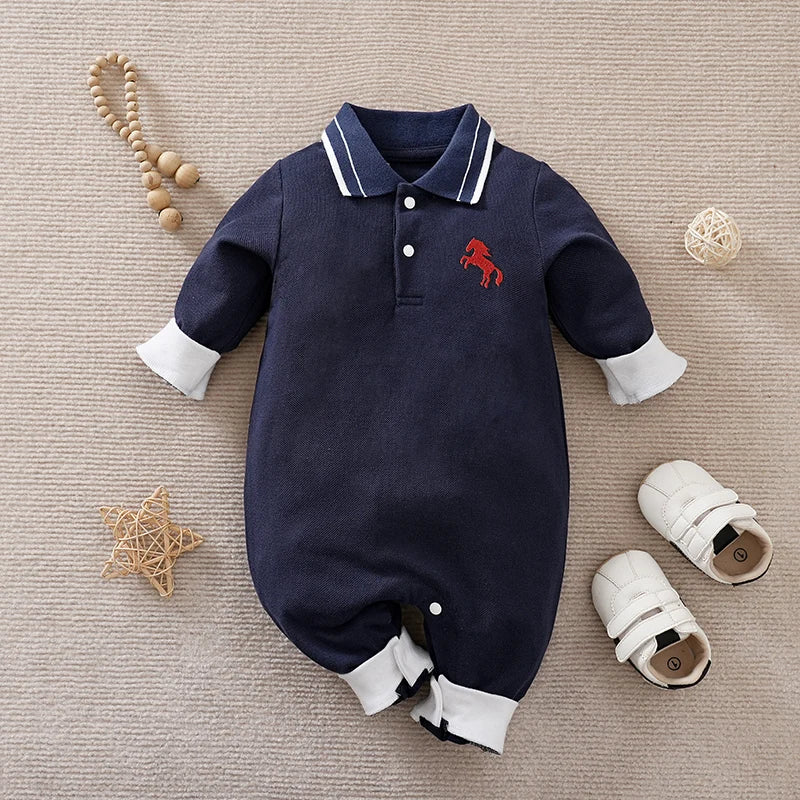 Navy baby romper with white trim and red horse emblem on a beige surface with baby items.