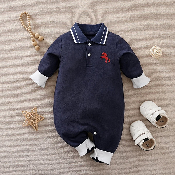 Navy baby romper with white trim and red horse emblem on a beige surface with baby items.