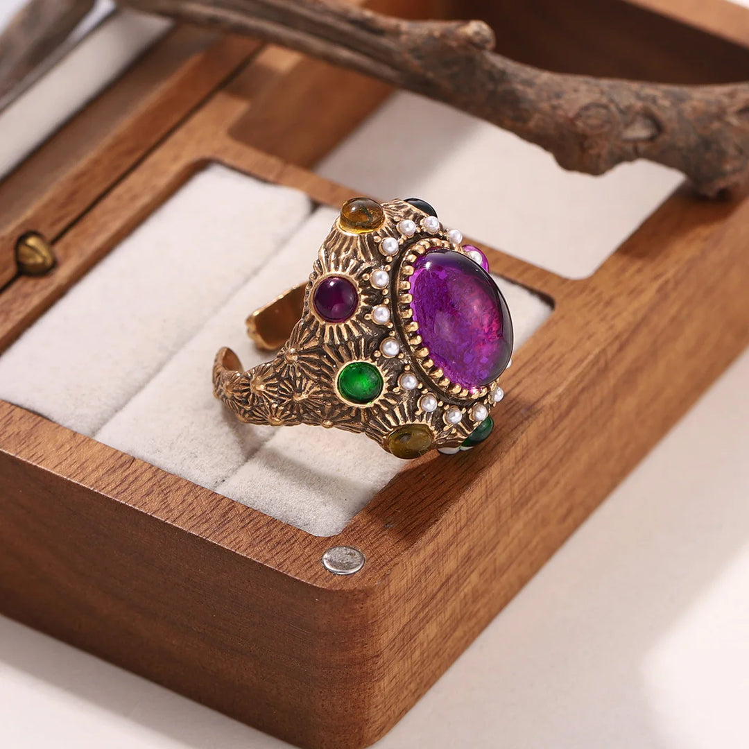 Baroque gold open ring with large oval purple stone, pearls, and green gem inlay