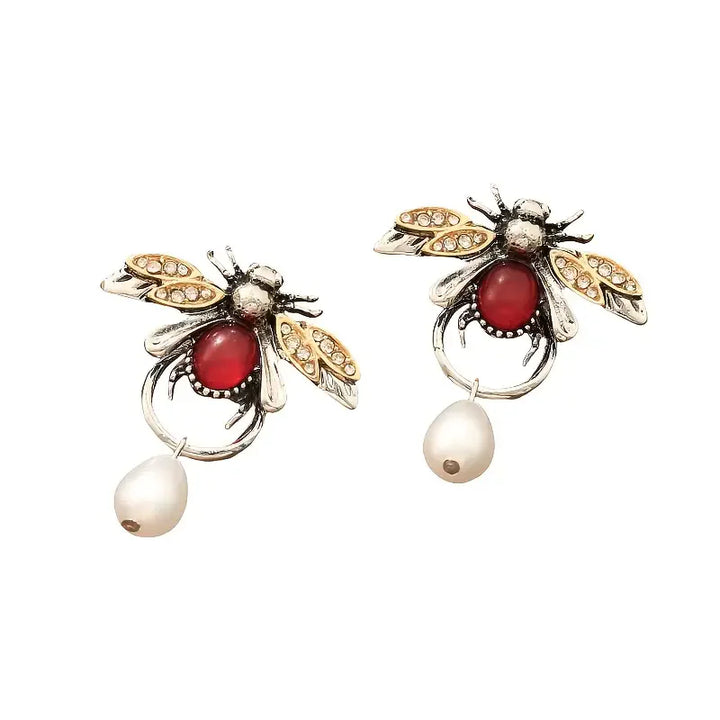 Bee-shaped earrings with red gemstones and pearl drops on a white background