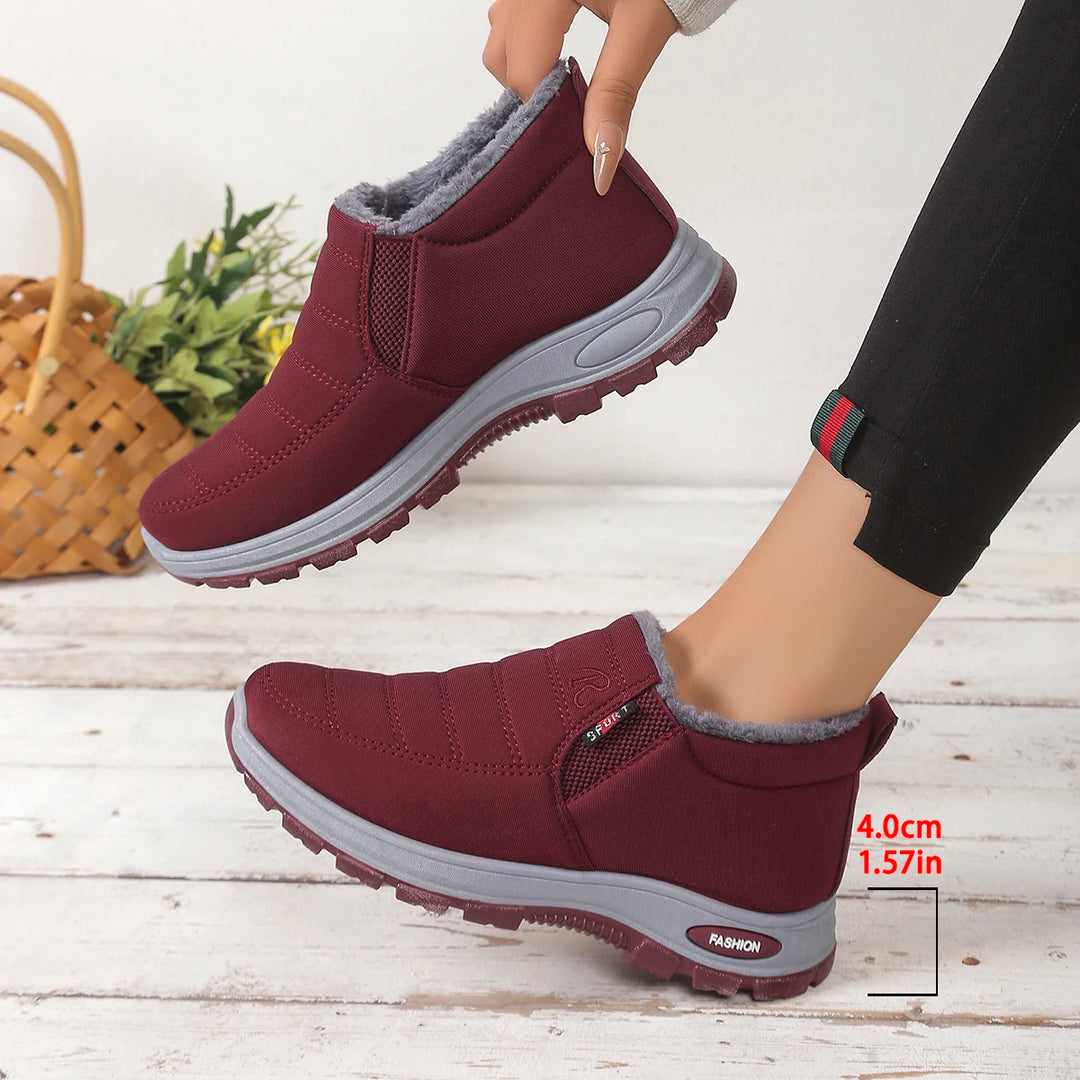 Maroon slip-on boots with gray soles on a light wooden floor.